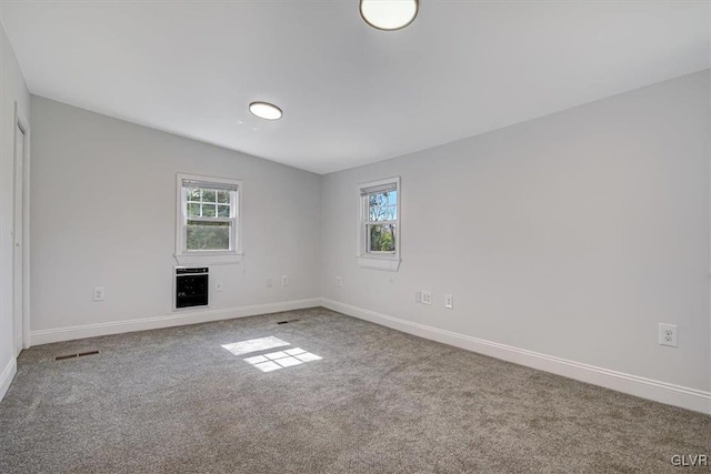 carpeted spare room with heating unit, vaulted ceiling, and plenty of natural light