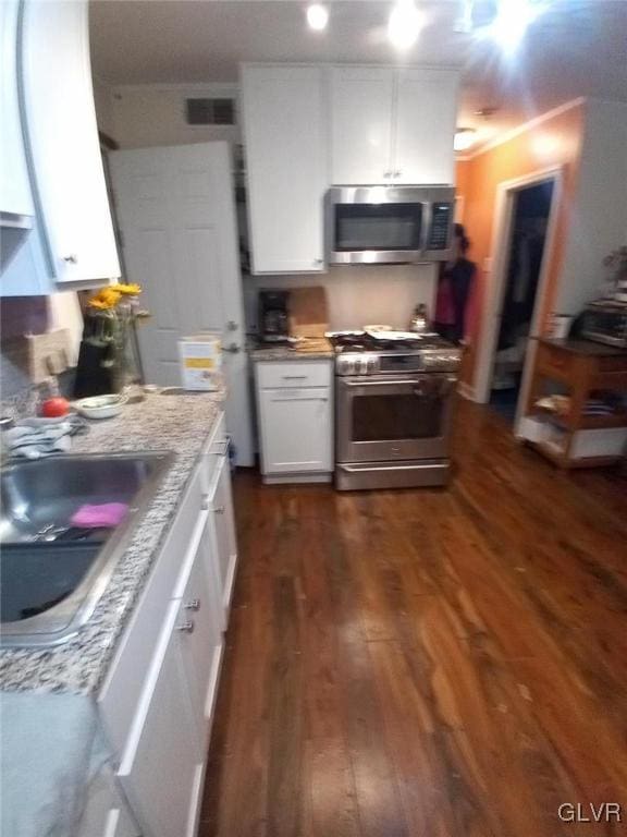 kitchen featuring dark wood-type flooring, stainless steel appliances, sink, light stone countertops, and white cabinetry