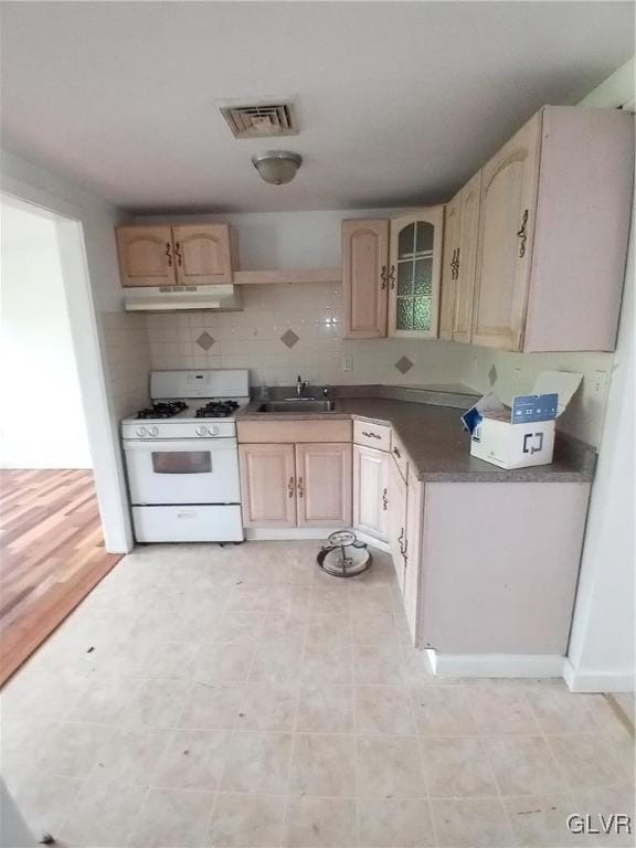 kitchen featuring sink, light brown cabinets, white gas range oven, and tasteful backsplash