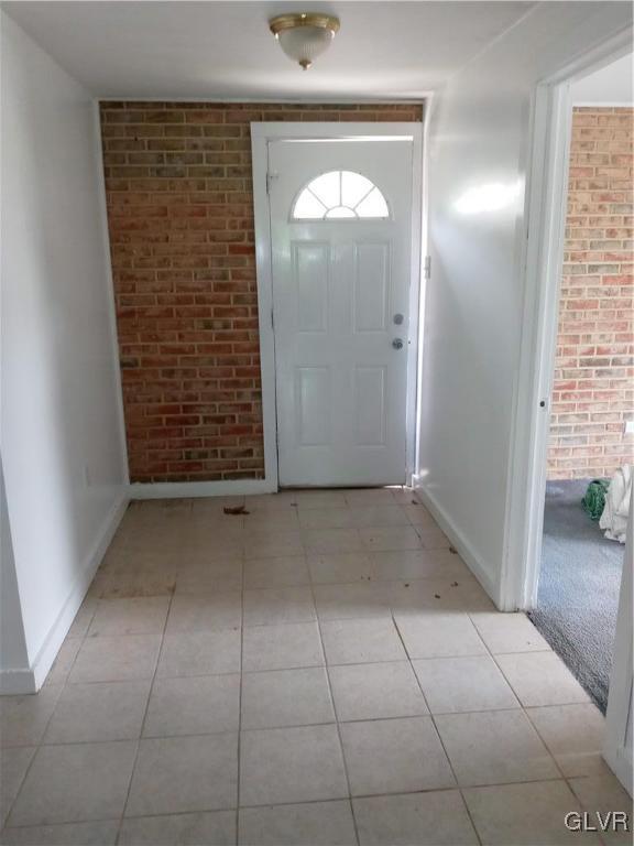 entrance foyer with light tile patterned floors, baseboards, and brick wall