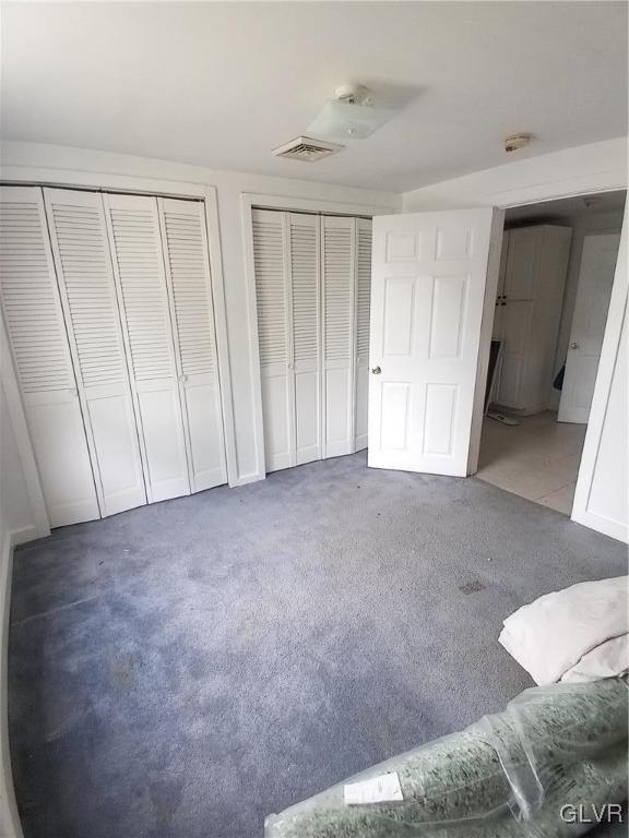 unfurnished bedroom featuring visible vents, carpet floors, and two closets