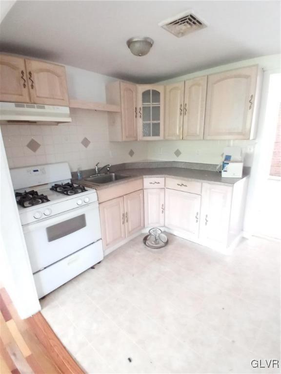 kitchen with light brown cabinets, visible vents, gas range gas stove, a sink, and under cabinet range hood