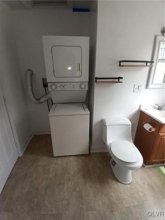 bathroom with vanity, stacked washer / drying machine, hardwood / wood-style flooring, and toilet