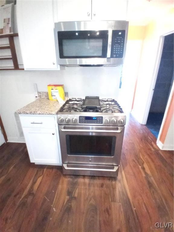 kitchen featuring light stone counters, appliances with stainless steel finishes, white cabinets, and dark wood-style flooring