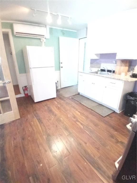 kitchen featuring a wall unit AC, freestanding refrigerator, wood finished floors, white cabinetry, and a sink