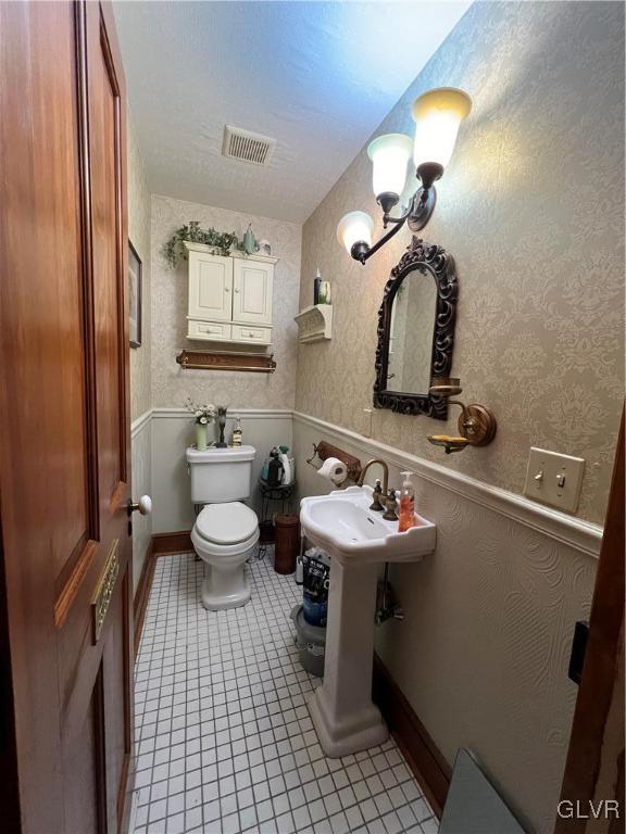 half bathroom featuring wainscoting, visible vents, toilet, and wallpapered walls