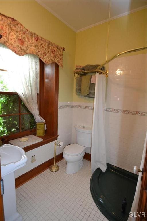 bathroom featuring toilet, a wainscoted wall, a tile shower, and ornamental molding