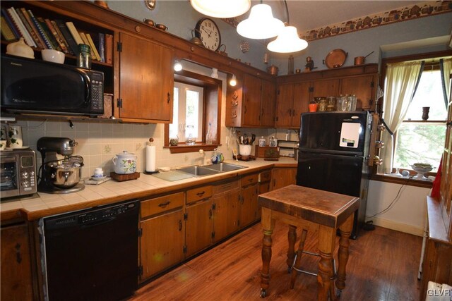 kitchen with tile countertops, black appliances, sink, hanging light fixtures, and light wood-type flooring