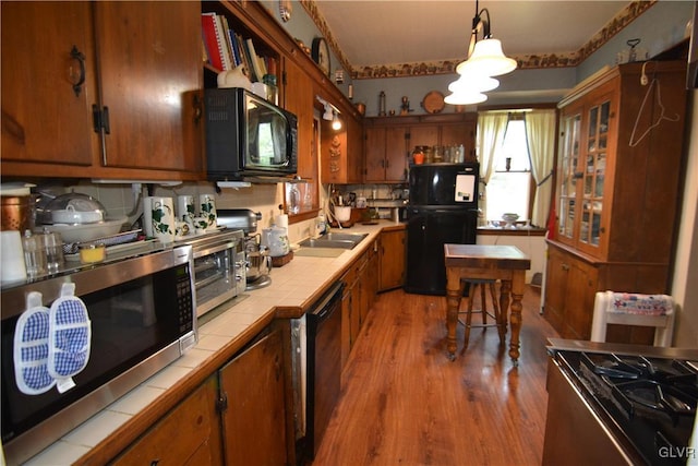 kitchen with black appliances, tile counters, backsplash, and hanging light fixtures