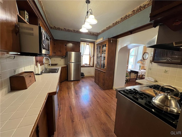 kitchen featuring dark wood-type flooring, a sink, arched walkways, appliances with stainless steel finishes, and tile counters