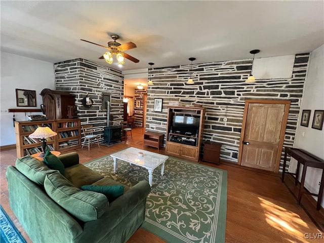 living room featuring wood finished floors, a wood stove, and a ceiling fan