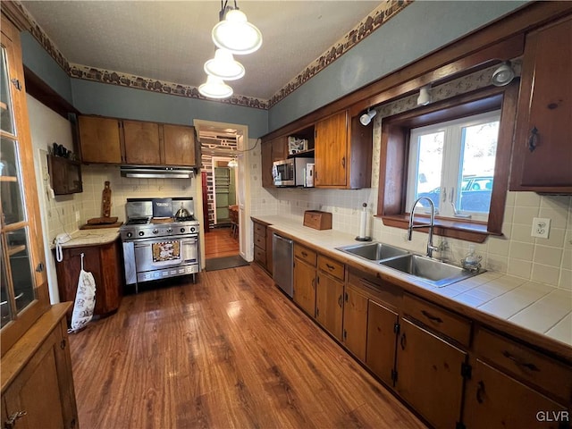 kitchen featuring a sink, stainless steel appliances, dark wood-type flooring, tile counters, and under cabinet range hood