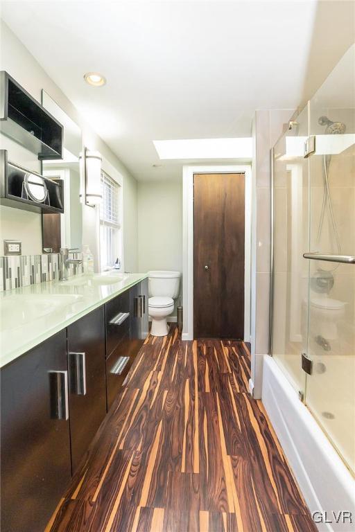 full bathroom with hardwood / wood-style floors, vanity, bath / shower combo with glass door, a skylight, and toilet