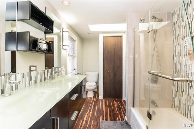 full bathroom featuring combined bath / shower with glass door, a skylight, vanity, hardwood / wood-style floors, and toilet