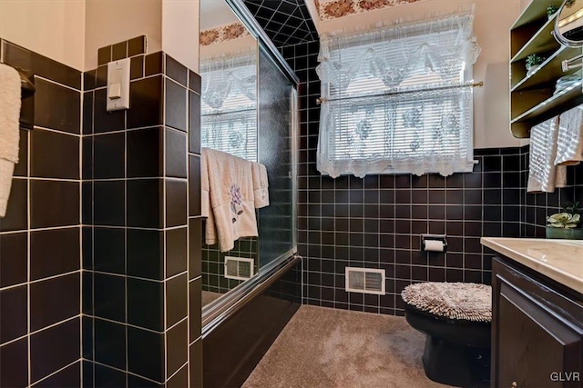 bathroom featuring toilet, plenty of natural light, a shower with shower door, and tile walls