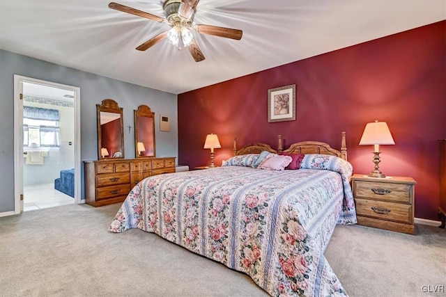 bedroom with ensuite bathroom, light carpet, and ceiling fan