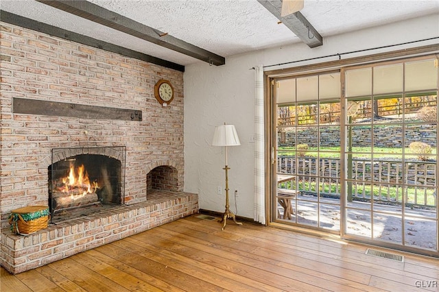 unfurnished living room with beam ceiling, hardwood / wood-style flooring, a textured ceiling, and a fireplace