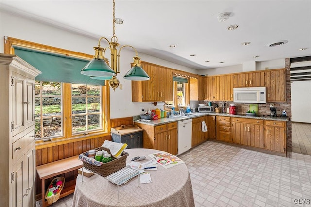 kitchen with decorative backsplash, wooden walls, sink, pendant lighting, and white appliances