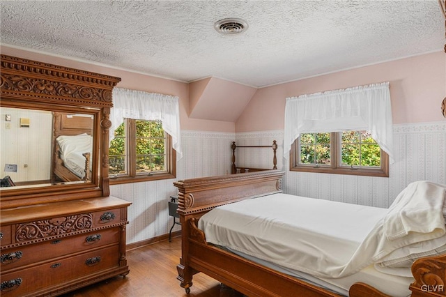 bedroom with multiple windows, a textured ceiling, hardwood / wood-style flooring, and vaulted ceiling