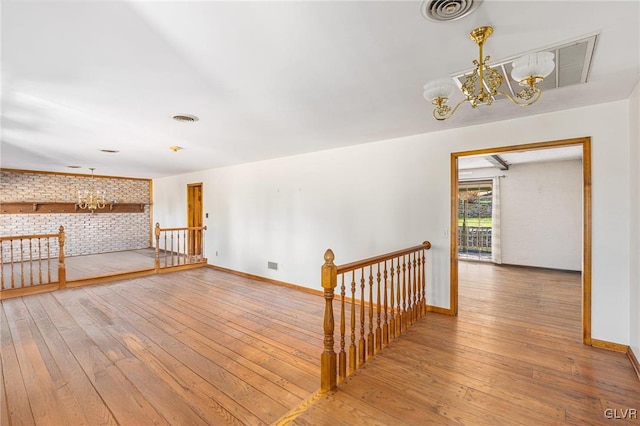 empty room featuring a notable chandelier, brick wall, and hardwood / wood-style floors