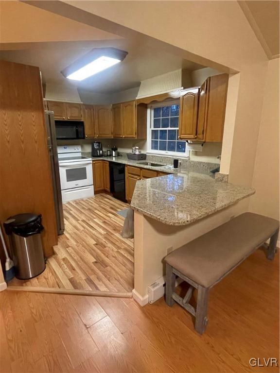 kitchen featuring light stone countertops, black appliances, light hardwood / wood-style flooring, and kitchen peninsula