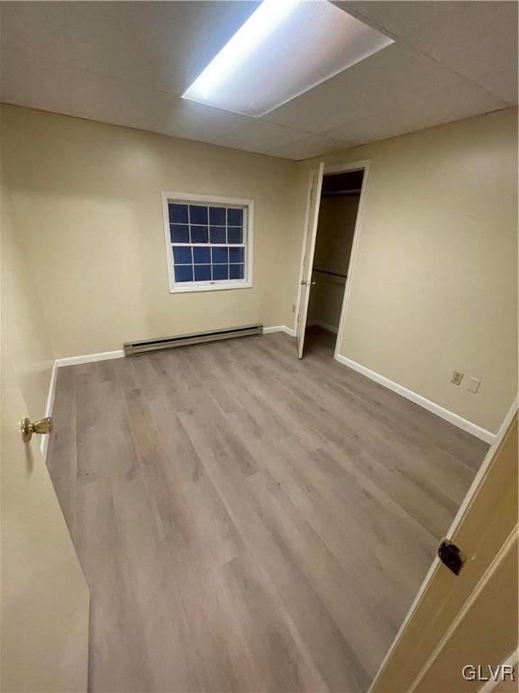 unfurnished bedroom with hardwood / wood-style floors, a baseboard heating unit, a drop ceiling, and a closet