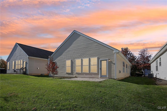 back house at dusk featuring cooling unit and a yard