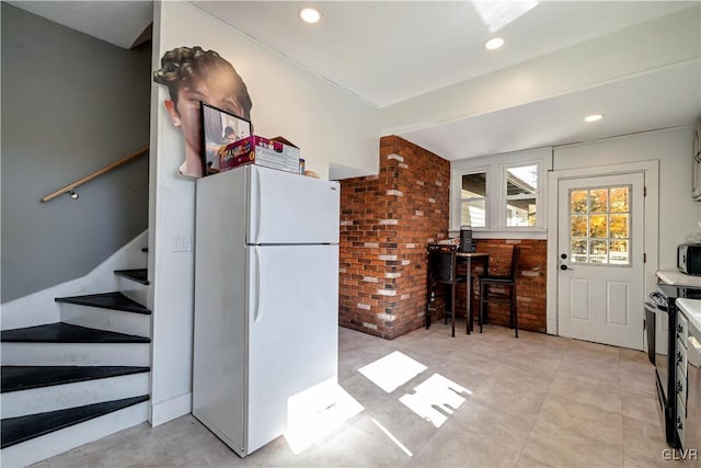 kitchen with black electric range, brick wall, and white refrigerator