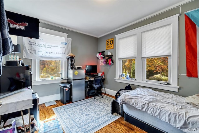 bedroom with crown molding, wood-type flooring, multiple windows, and stainless steel fridge