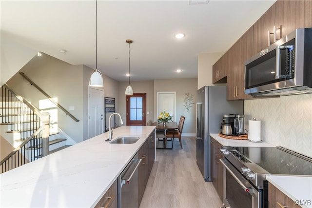 kitchen with decorative backsplash, appliances with stainless steel finishes, light hardwood / wood-style flooring, pendant lighting, and sink