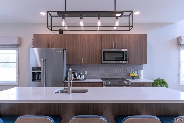 kitchen featuring decorative backsplash, a kitchen bar, sink, pendant lighting, and stainless steel appliances