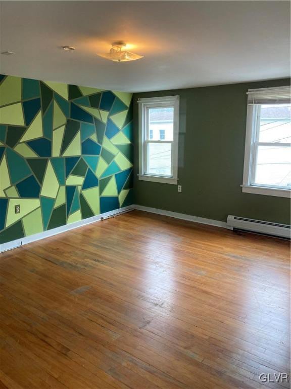 empty room featuring hardwood / wood-style flooring, a baseboard radiator, and plenty of natural light