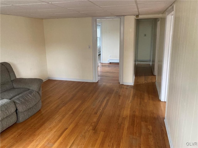 living room with a baseboard heating unit, wood-type flooring, and a paneled ceiling