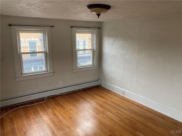 empty room featuring light hardwood / wood-style flooring, a baseboard heating unit, a healthy amount of sunlight, and a textured ceiling