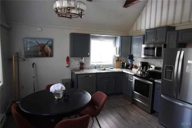 kitchen with wood-type flooring, vaulted ceiling, sink, gray cabinetry, and stainless steel appliances