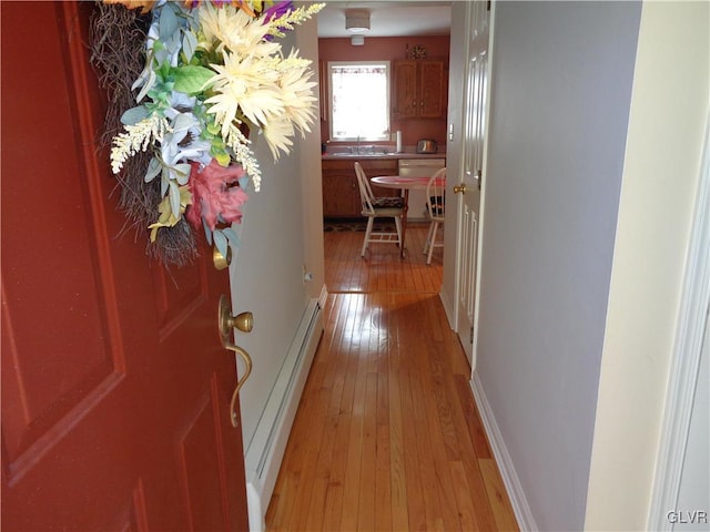 hall featuring sink, a baseboard heating unit, and light hardwood / wood-style floors