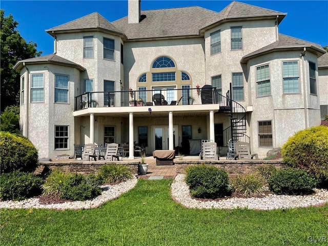 rear view of house with a balcony, a yard, and a patio