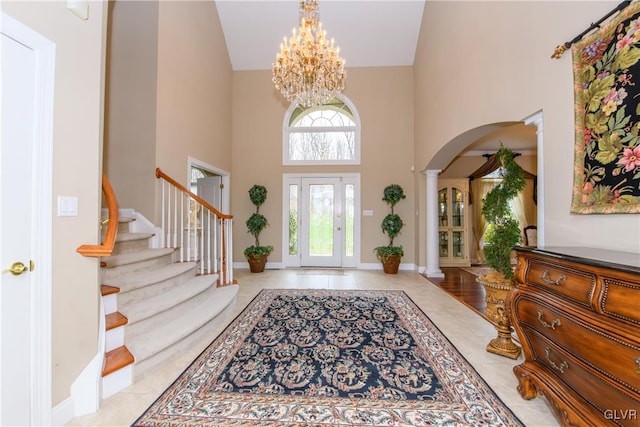 entrance foyer featuring a notable chandelier, light tile patterned flooring, a towering ceiling, and decorative columns