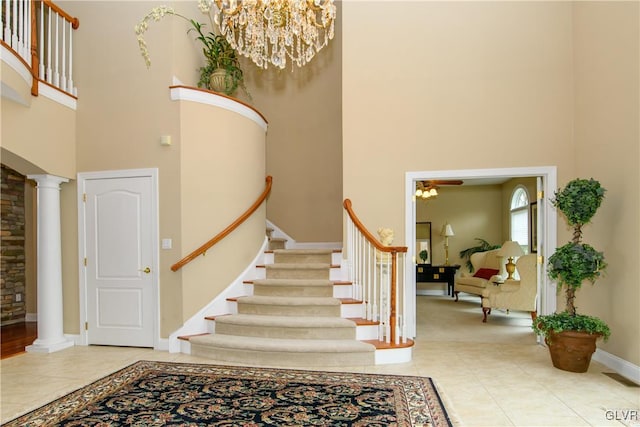 staircase with ornate columns, tile patterned flooring, a towering ceiling, and a notable chandelier