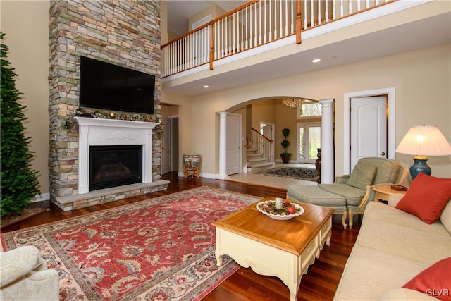 living room with a towering ceiling, dark hardwood / wood-style floors, ornate columns, and a stone fireplace