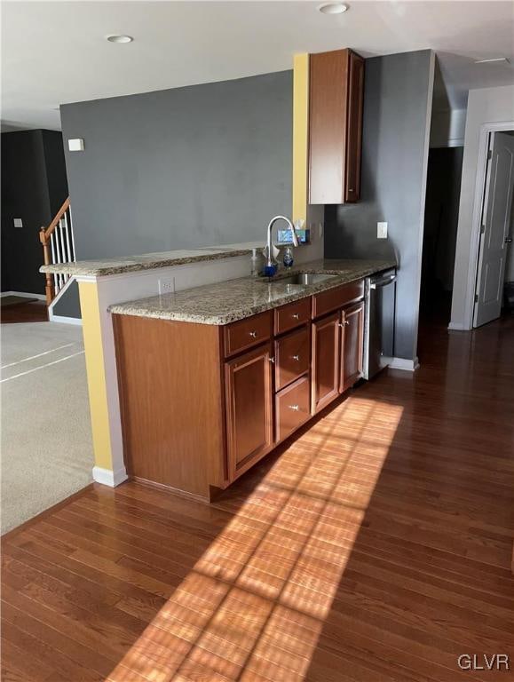 kitchen featuring light stone countertops, sink, kitchen peninsula, stainless steel dishwasher, and dark wood-type flooring