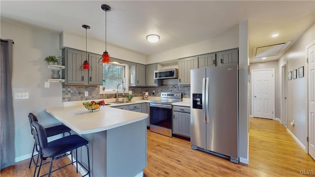 kitchen with kitchen peninsula, appliances with stainless steel finishes, a kitchen bar, pendant lighting, and light hardwood / wood-style floors