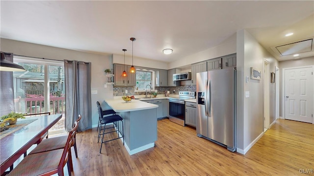 kitchen featuring appliances with stainless steel finishes, hanging light fixtures, light wood-type flooring, and a wealth of natural light