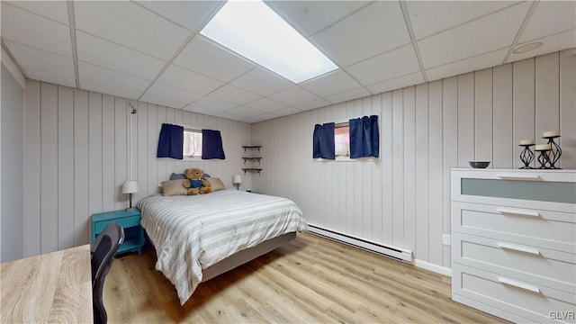 bedroom featuring baseboard heating, a drop ceiling, light hardwood / wood-style floors, and wooden walls