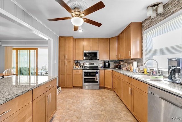 kitchen featuring crown molding, appliances with stainless steel finishes, sink, backsplash, and light stone counters