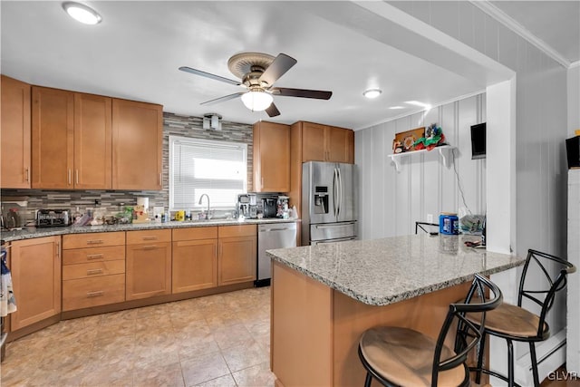 kitchen with a breakfast bar area, sink, crown molding, light stone countertops, and appliances with stainless steel finishes