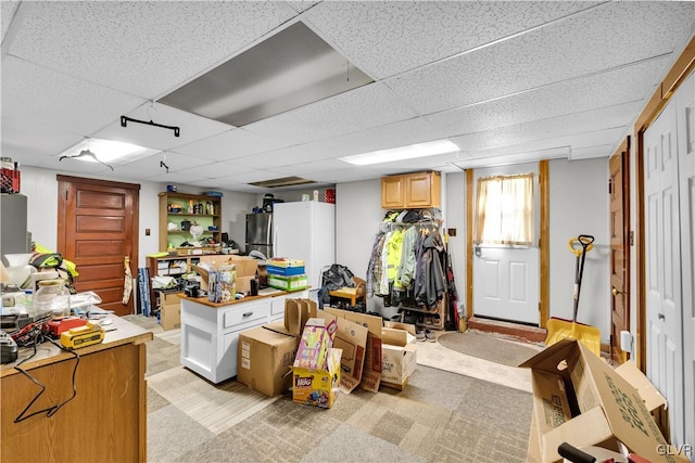 basement with a paneled ceiling, light colored carpet, and stainless steel refrigerator