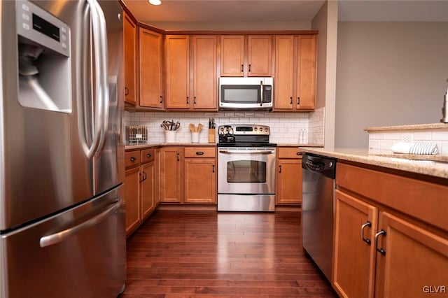 kitchen with light stone countertops, appliances with stainless steel finishes, dark hardwood / wood-style floors, and tasteful backsplash