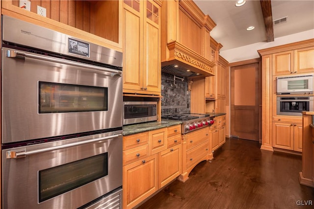 kitchen featuring decorative backsplash, dark wood-type flooring, dark stone countertops, custom exhaust hood, and appliances with stainless steel finishes