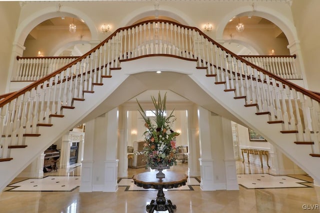 staircase with decorative columns, a chandelier, a high ceiling, and ornamental molding